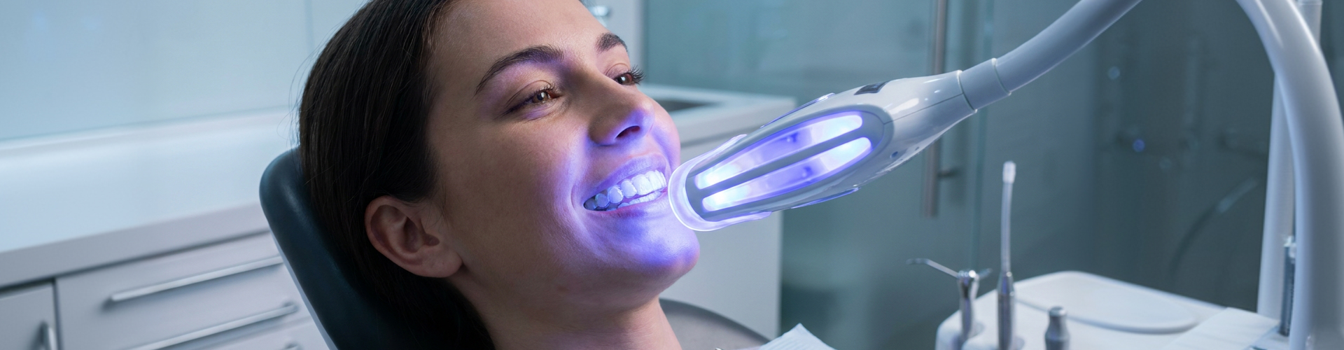 Woman receiving professional teeth whitening treatment while wearing clear Invisalign aligner trays.